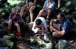 Matthew and Colin watch John use the pestle on the mortar stone at Week Ford Blowing House